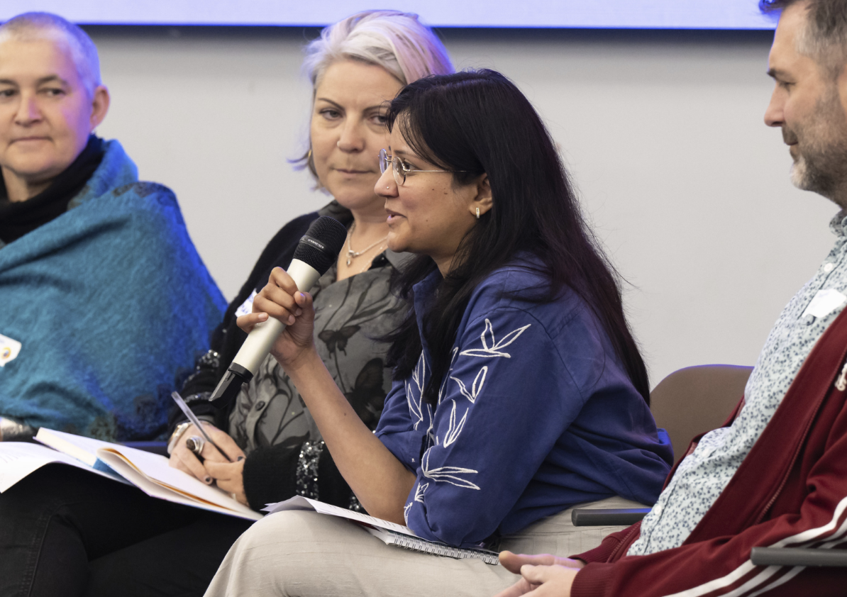 a conference panel discussion of four people, a lady is holding the microphone and the others are listening