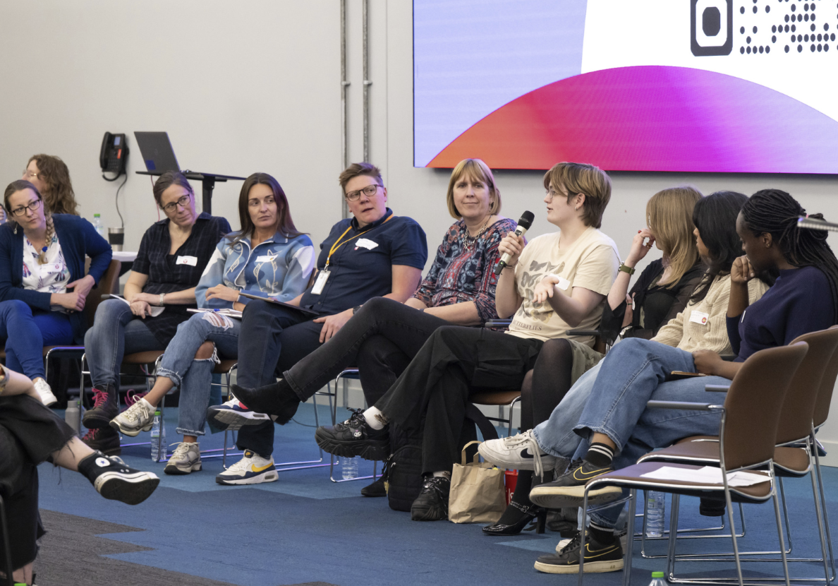 a row of 10 people on chairs forming a conference panel session, one student is holding a microphone while the others listen to her