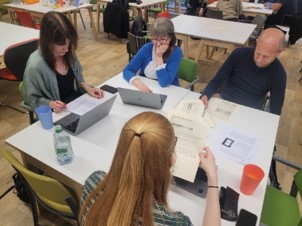 Photograph of four people sitting at a classroom-style table reading printed articles.