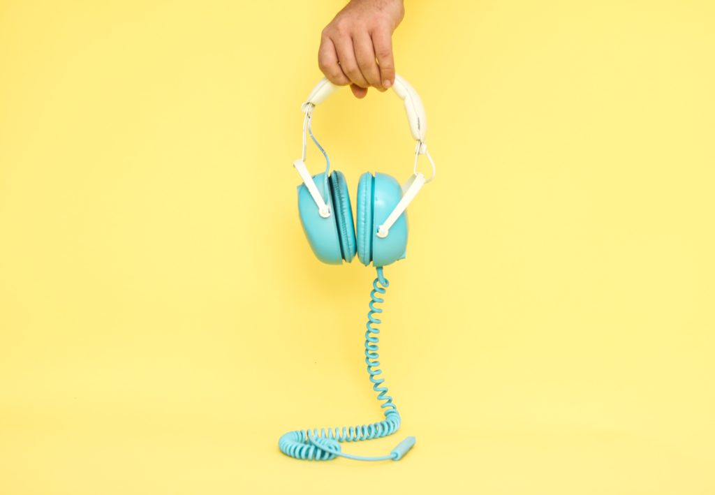 Blue headphones being held over yellow background with cord trailing.