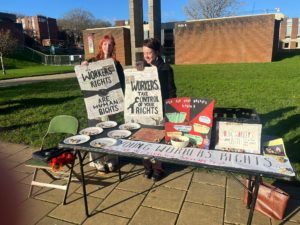 Photograph of two students on Sussex campus campaigning for young workers rights through newspapers and flyers and activities. 