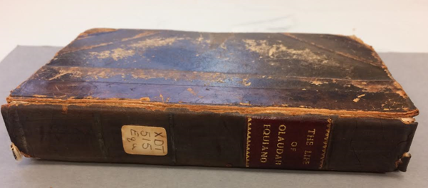 A closed book resting on it's side. The cover is brown leather and the title 'The life of Olaudah Equiano' is visible. The book is damaged.