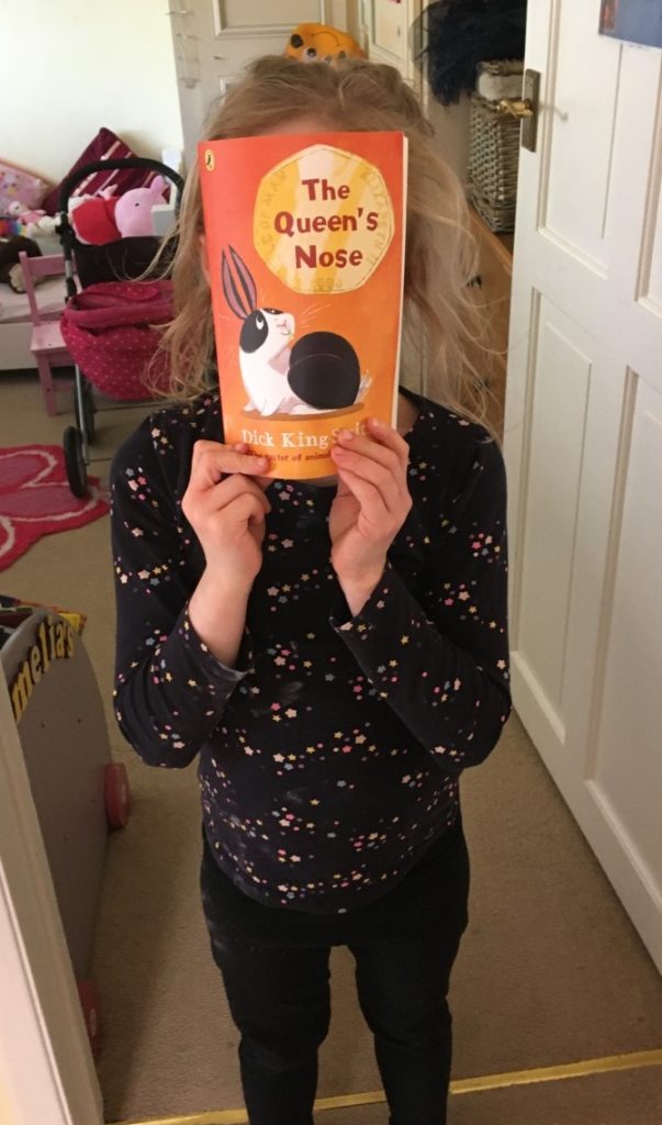 A child holding up a copy of the book The Queen's Nose.