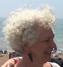 Profile photo of blog post author Sue Robbins. She looks off camera to the right, standing on front of the sea.