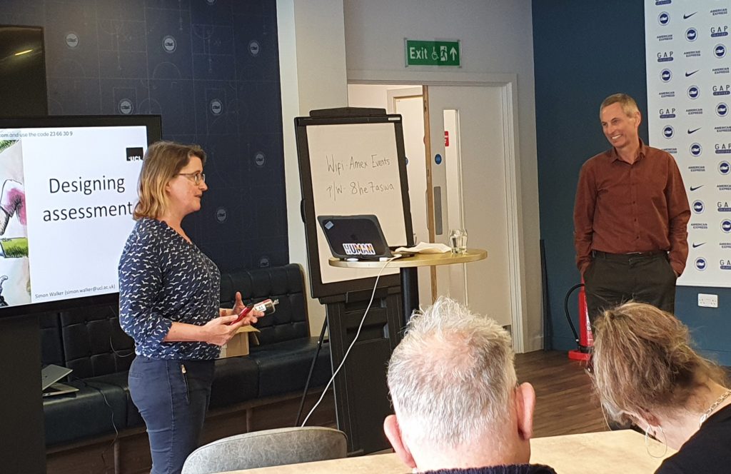 Katie Piatt introducing Prof Simon Walker. Katie is in front of a screen showing a slide labelled 'Designing Assessment'. Members of the audience can be seen watching.