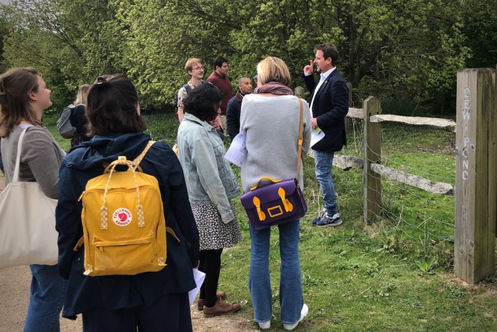 Group of 9 attendees outdoors near a fence with the sign 'Dew Pond'