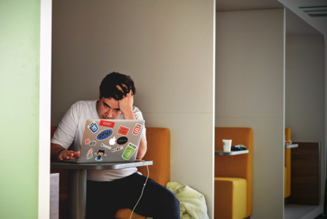 A photo of a young man, head in his hands in front of a laptop, representing a student feeling frustrated with an assignment.