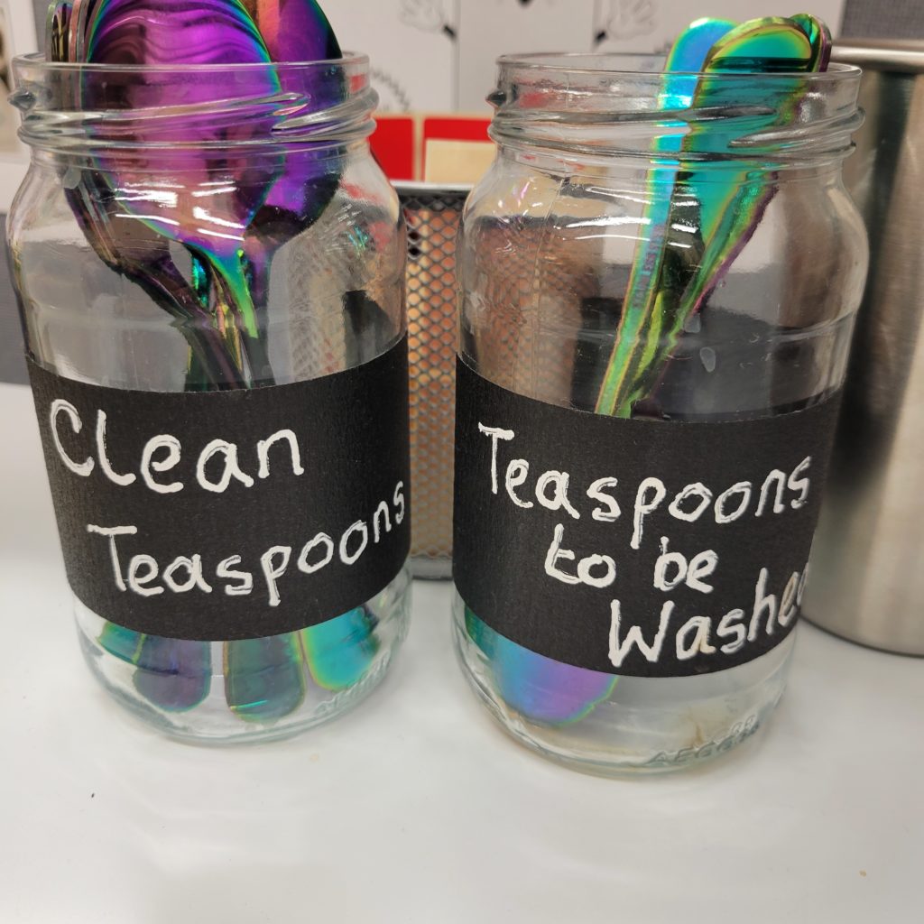 Two recycled glass jars, one labelled "clean teaspoons" and the other "teaspoons to be washed".